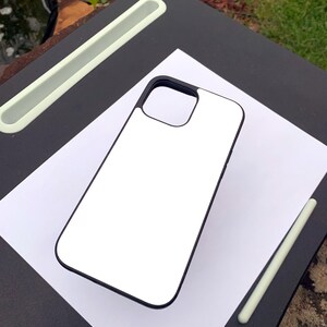 Puede incluir: Una funda de tel&eacute;fono blanca con borde negro, sobre una hoja de papel blanca. Un l&aacute;piz &oacute;ptico verde claro y un escritorio negro con una ranura verde claro tambi&eacute;n son visibles. La funda est&aacute; en blanco.