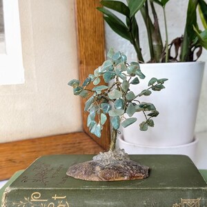 May include: A jade green gemstone tree sculpture on a wooden base, sitting on top of two green books. The books are titled "The Secret Garden" and "A Trip East".