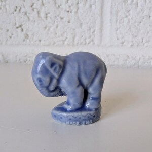 May include: A small, light blue ceramic elephant figurine. The elephant is in a downward pose, with its trunk touching the ground. The base has a decorative pattern and the text "WADE ENG".