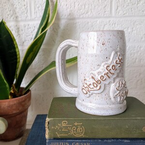 May include: White ceramic beer stein with brown speckled glaze. The stein has the words "Oktoberfest Est. 1969" embossed on the side.