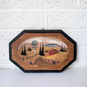 May include: An octagonal wooden wall hanging with a landscape painting. The painting shows a red house, trees, and a road, with the text "Halifax, N.S." at the bottom. The frame is black with a brown interior.
