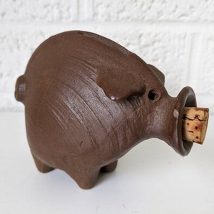 May include: A brown ceramic pig bottle stopper with a cork in its mouth.