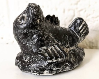 May include: A black and white carved stone sculpture of a seal. The seal is lying on its side with its head tilted up. The sculpture is detailed and realistic.