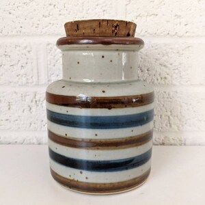 May include: A ceramic jar with a cork lid. The jar has a white base with brown and blue stripes.