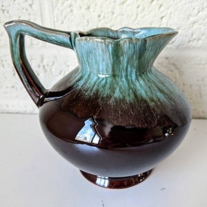 May include: A brown and blue glazed ceramic pitcher with a flared lip and a rounded body. The pitcher has a handle and a base.