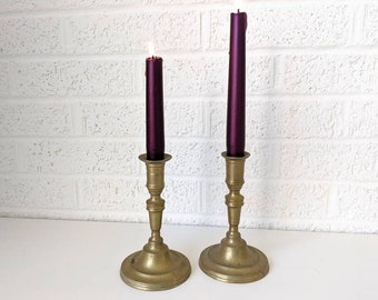 Può includere: Due candelabri in ottone con candele color borgogna. Le candele sono accese e i candelabri hanno un design classico.