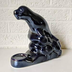 May include: A black ceramic incense burner shaped like a seal sitting on a rock. The burner has a small dish for incense.