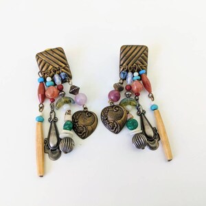 May include: A pair of dangle earrings featuring a mix of colourful beads, including turquoise, red, green, and pink. The earrings have a heart-shaped charm and a long, wooden bead.