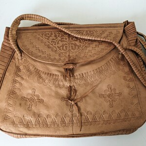 Puede incluir: Un bolso de cuero marr&oacute;n con intrincados dise&ntilde;os en relieve. El bolso tiene un cierre de solapa y una correa larga.