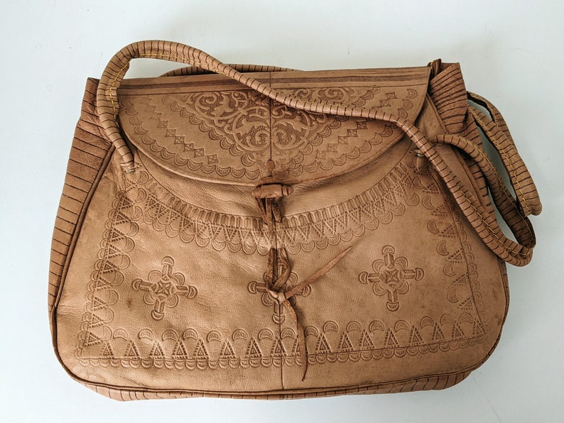 Puede incluir: Un bolso de cuero marr&oacute;n con intrincados dise&ntilde;os en relieve. El bolso tiene un cierre de solapa y una correa larga.