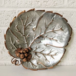 May include: A silver and copper leaf-shaped serving dish with a grape cluster design. The dish is made of metal and has a hammered texture.
