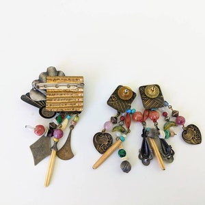 May include: A pair of dangle earrings and a brooch with a gold and silver finish. The earrings and brooch feature a variety of colourful beads, charms, and pendants.
