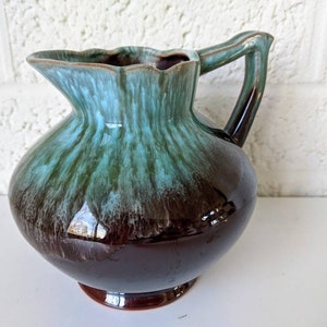 May include: A brown and green glazed ceramic pitcher with a flared lip and a handle. The pitcher has a mottled glaze with shades of brown, green, and blue.