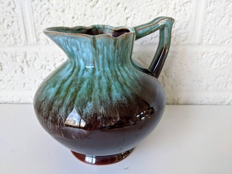 May include: A brown and green glazed ceramic pitcher with a flared lip and a handle. The pitcher has a mottled glaze with shades of brown, green, and blue.