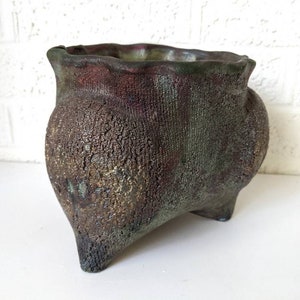 May include: A dark green and brown ceramic planter with a textured surface and three legs.