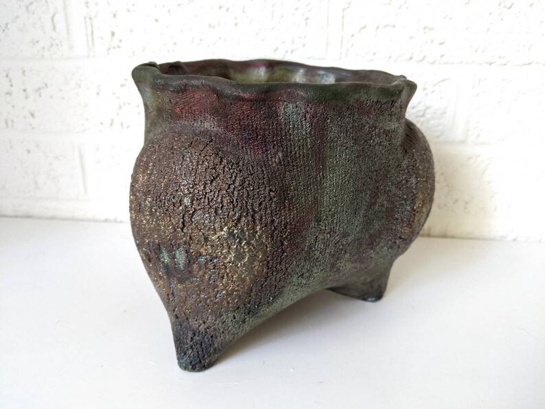 May include: A dark green and brown ceramic planter with a textured surface and three legs.