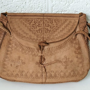 Puede incluir: Un bolso de cuero marr&oacute;n con intrincados dise&ntilde;os en relieve. El bolso tiene un cierre de solapa con una correa de cuero anudada.