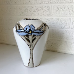 May include: White ceramic vase with a blue and brown floral design. The vase has a wide mouth and a narrow base.