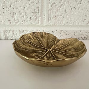 May include: A gold leaf-shaped dish with a textured surface. The dish is made of metal and has a slightly curved shape.