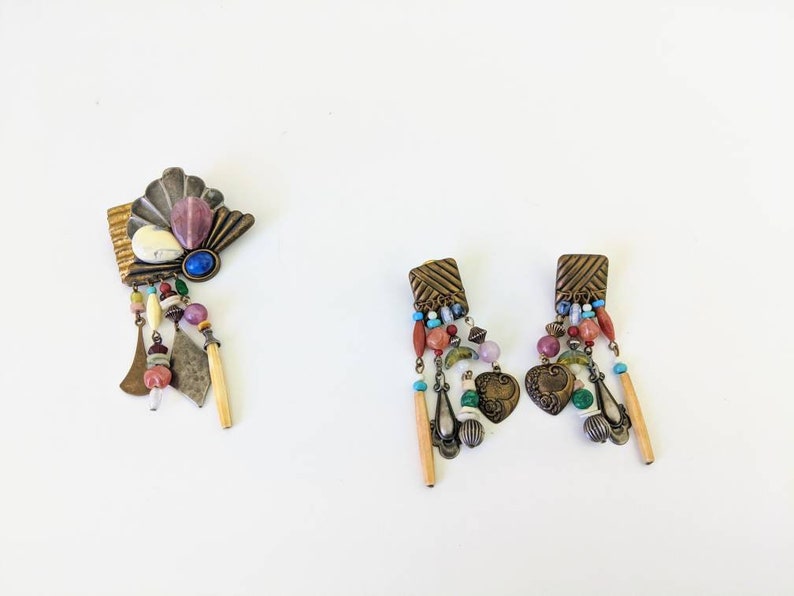 May include: A set of earrings and a brooch in a bohemian style. The jewellery features a mix of colourful beads, metal charms, and natural elements. The earrings are long and dangle, while the brooch is a statement piece with a fan-shaped design.