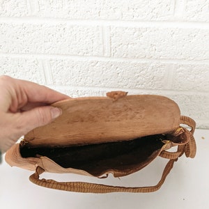 Puede incluir: Un bolso de mano de cuero marr&oacute;n con una correa larga. El bolso est&aacute; abierto y el interior es visible.