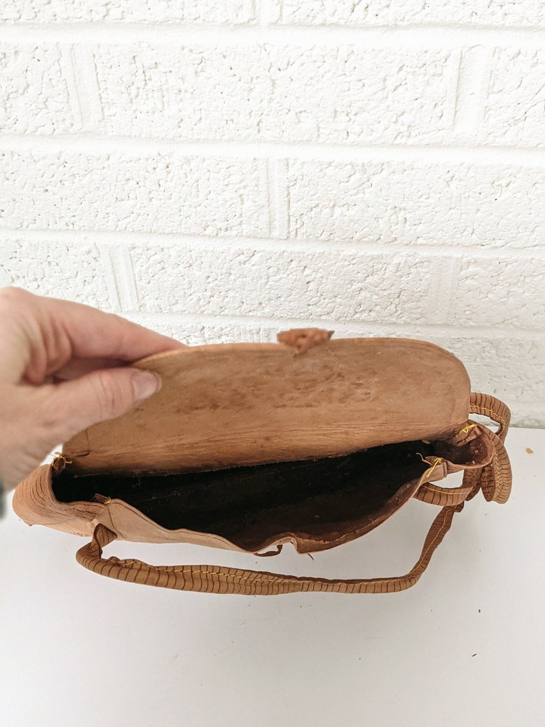 Puede incluir: Un bolso de mano de cuero marr&oacute;n con una correa larga. El bolso est&aacute; abierto y el interior es visible.