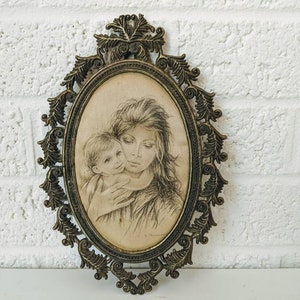 May include: A vintage oval-shaped picture frame with an ornate gold metal design. The frame holds a black and white drawing of a mother and child.