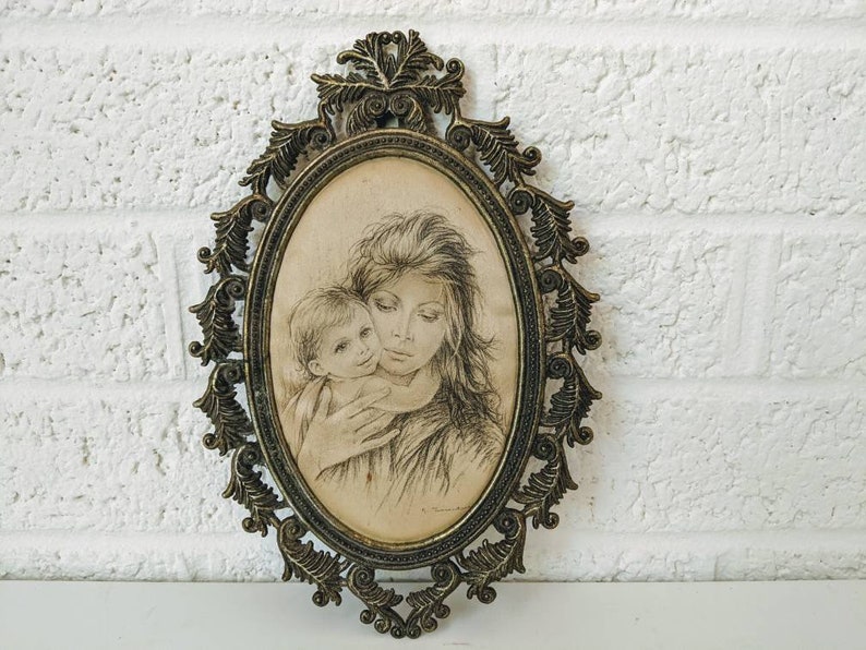 May include: A vintage oval-shaped picture frame with an ornate gold metal design. The frame holds a black and white drawing of a mother and child.