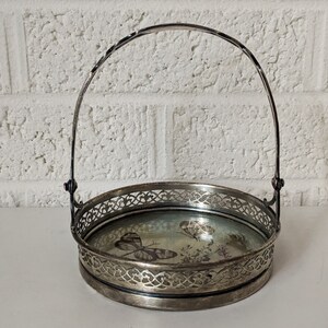 May include: A silver serving basket with a glass bottom and a decorative handle. The glass bottom features a floral design with butterflies.