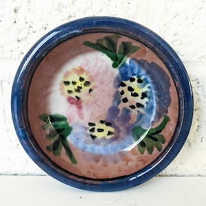Puede incluir: Un pequeño cuenco redondo de cerámica con un borde azul y un diseño floral. El cuenco está pintado con flores rosas, azules, amarillas y verdes.