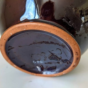 May include: The bottom of a dark brown ceramic vase with a terracotta rim. The vase has a white mark that reads "G 40".
