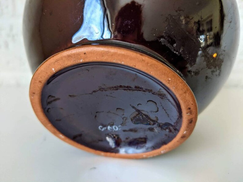 May include: The bottom of a dark brown ceramic vase with a terracotta rim. The vase has a white mark that reads "G 40".