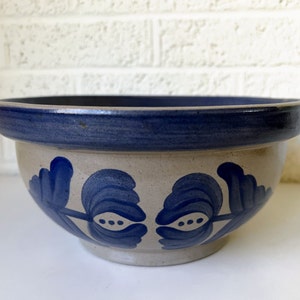 May include: A large, stoneware bowl with a blue rim and blue floral design. The bowl is made in a rustic style and has a light brown glaze.