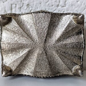May include: Silver metal trinket box with a decorative, textured design and four small feet on the bottom.