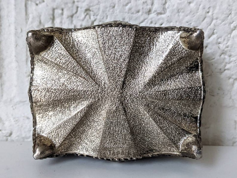 May include: Silver metal trinket box with a decorative, textured design and four small feet on the bottom.