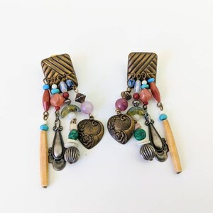 May include: A pair of dangle earrings with a brass base and a variety of colourful beads, including turquoise, red, green, and pink. The earrings feature a heart-shaped charm with floral details.