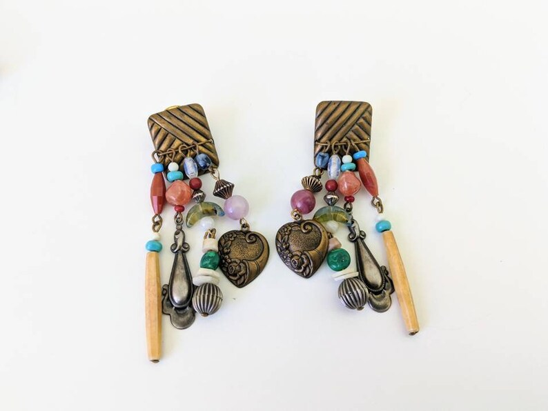 May include: A pair of dangle earrings with a brass base and a variety of colourful beads, including turquoise, red, green, and pink. The earrings feature a heart-shaped charm with floral details.