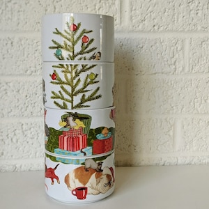 May include: A stack of four white ceramic bowls. Each bowl features a different Christmas-themed illustration. The designs include a Christmas tree, wrapped gifts, cats, and a bulldog. The bowls are stacked on top of each other.
