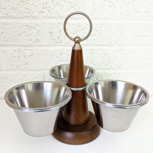 Könnte beinhalten: Ein Holz-Gewürzständer mit einem silbernen Ringgriff und drei Schalen aus Edelstahl. Der Ständer ist braun und hat eine konische Form.