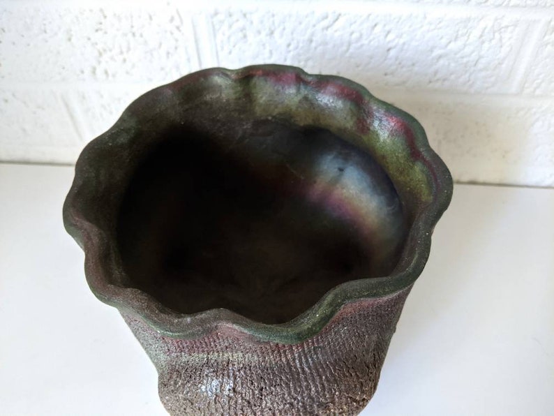 May include: A dark green and brown ceramic planter with a wavy rim. The planter has a textured surface and a slightly iridescent finish.