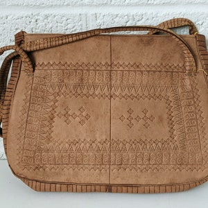 Puede incluir: Un bolso de hombro de cuero marr&oacute;n con intrincados patrones en relieve. El bolso tiene un cierre de solapa y una correa larga.