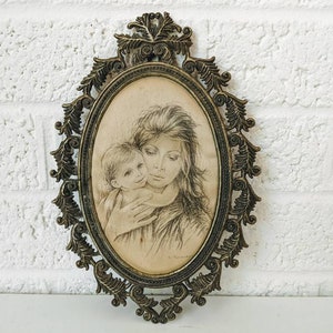 May include: A vintage oval-shaped picture frame with an ornate gold metal design. The frame holds a black and white drawing of a mother and child.