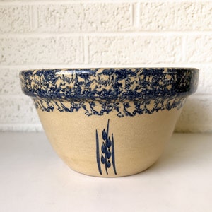 May include: A large, cream-colored ceramic mixing bowl with a blue and white speckled glaze. The bowl has a blue wheat design on the front.