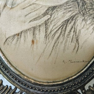 May include: A vintage oval-shaped framed drawing of a woman's face with a silver frame and a beaded border. The drawing is signed "G. Caventou".