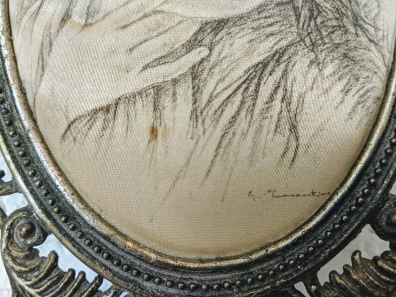May include: A vintage oval-shaped framed drawing of a woman's face with a silver frame and a beaded border. The drawing is signed "G. Caventou".