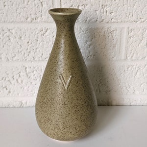 May include: A speckled green ceramic vase with a white 'V' on the front.