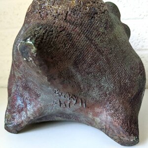 May include: A dark brown, textured ceramic sculpture with a rough, uneven surface. The sculpture is signed "Becky Smith" on the bottom.