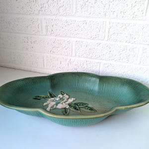 Puede incluir: Un plato de servir de cer&aacute;mica verde con un dise&ntilde;o de flor blanca en relieve. El plato tiene un borde festoneado y es perfecto para servir aperitivos o aperitivos.