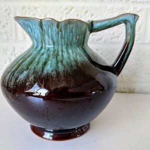 May include: A brown and teal glazed ceramic pitcher with a flared lip and a handle. The pitcher has a glossy finish and a unique swirl pattern.