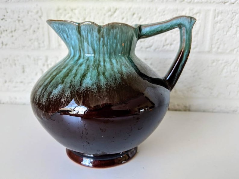 May include: A brown and teal glazed ceramic pitcher with a flared lip and a handle. The pitcher has a glossy finish and a unique swirl pattern.